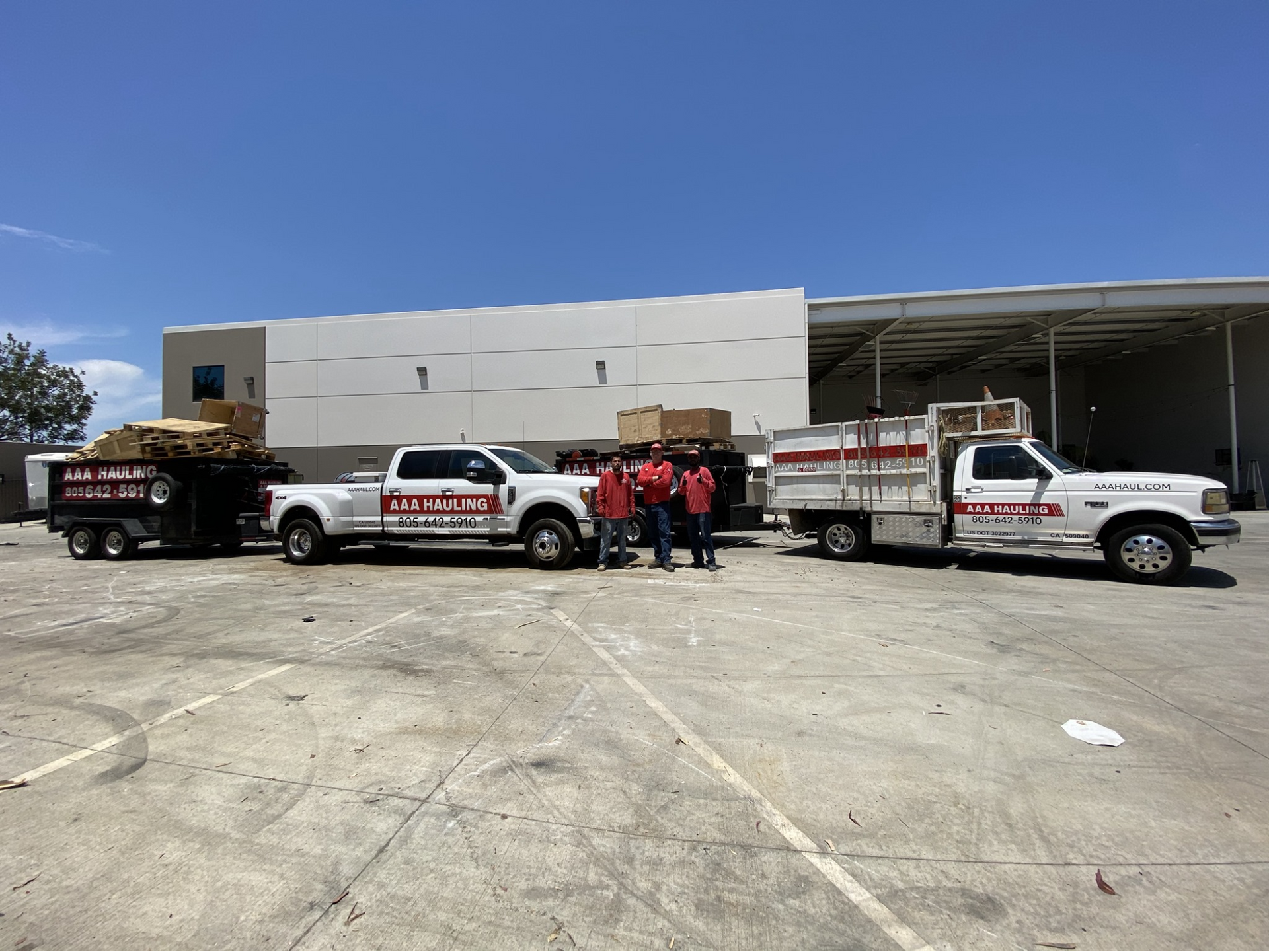 A group of trucks are parked in a parking lot in front of a building with three people in front