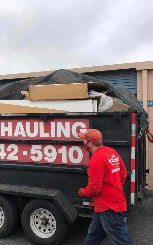 a man in a red shirt is pushing a dumpster full of junk .