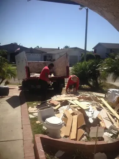 Two men are working on a toilet in front of a dumpster.