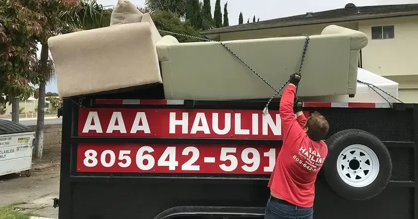 A man is loading a couch into a dump truck