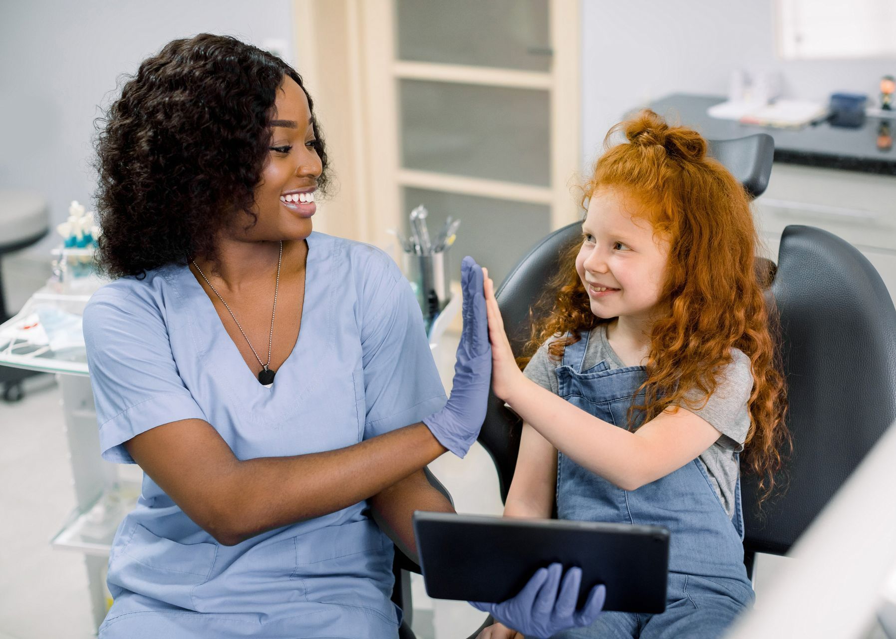 A dentist and a little girl are giving each other a high five in a dental office.