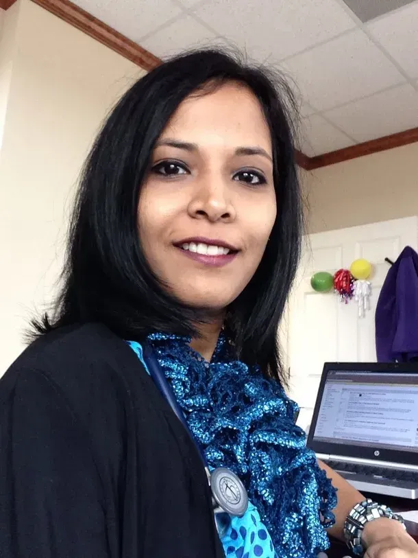 A woman with a stethoscope around her neck is smiling in front of a laptop