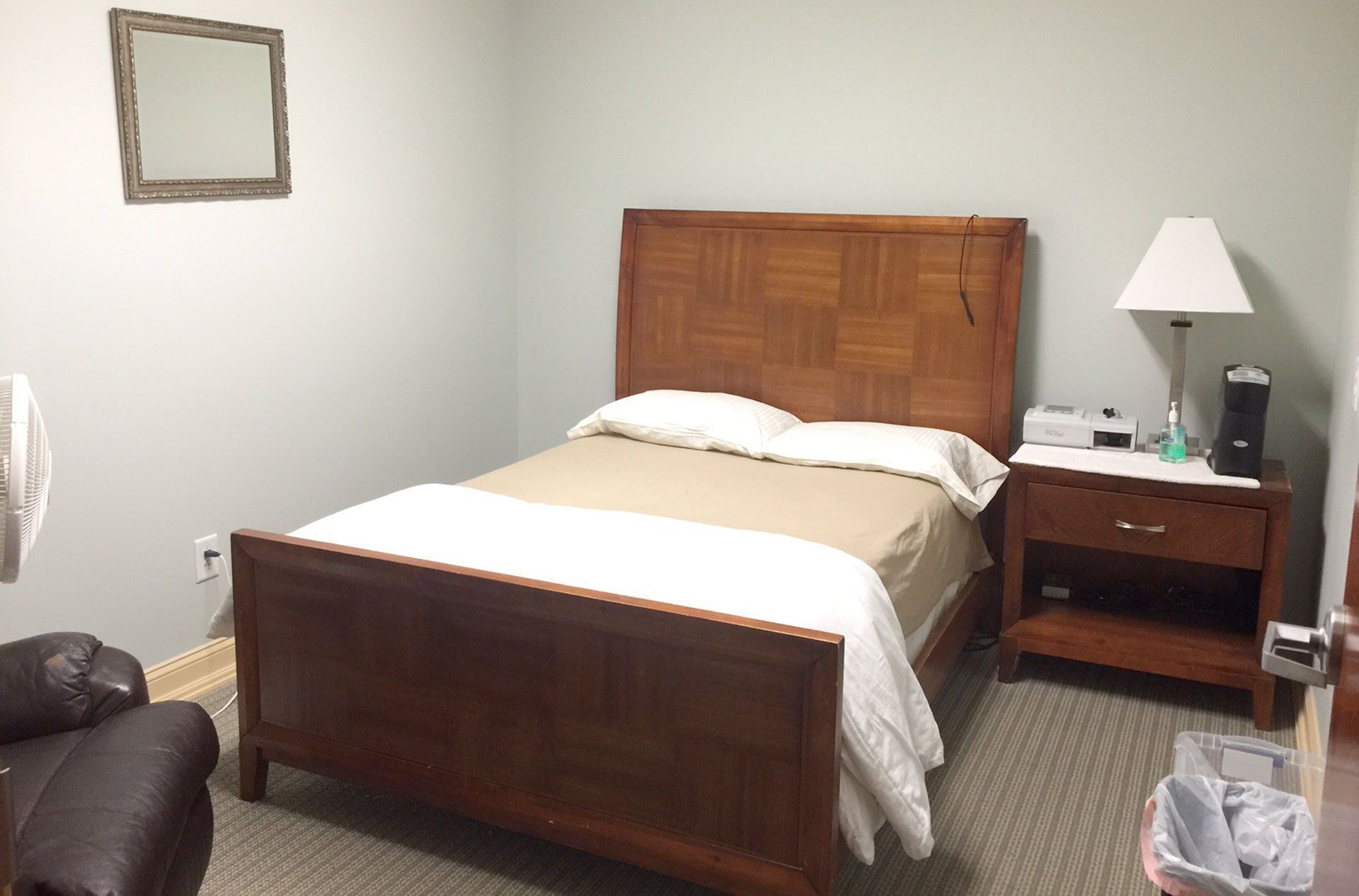 A bedroom with a bed , nightstand , lamp and mirror