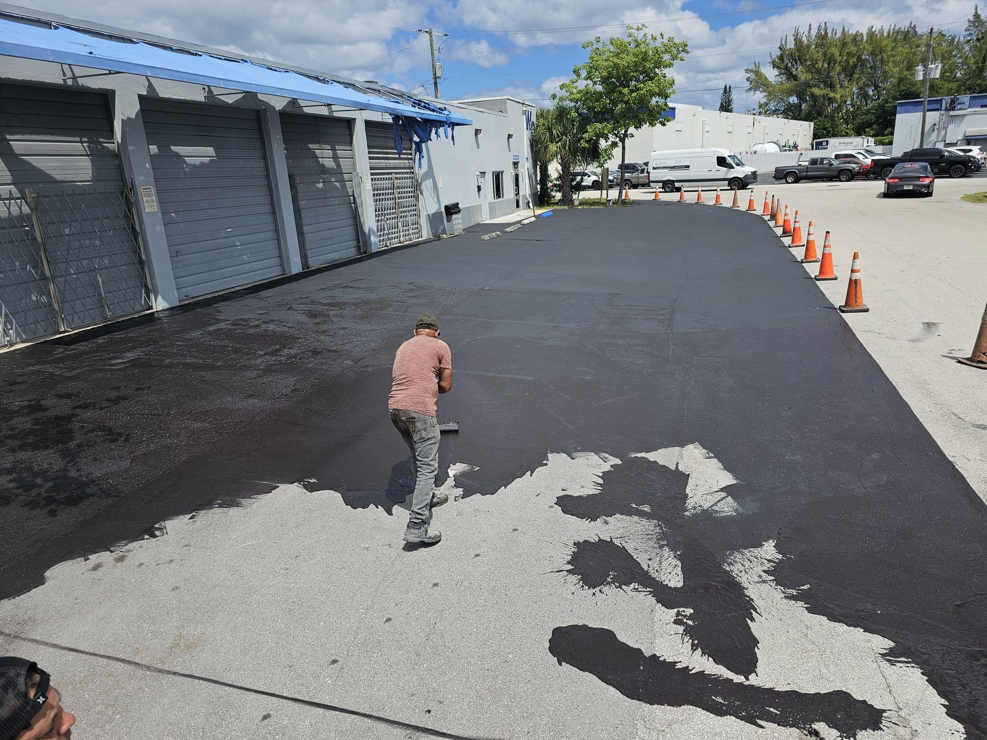 Person applying driveway sealer with a brush to protect and enhance the surface of the asphalt.