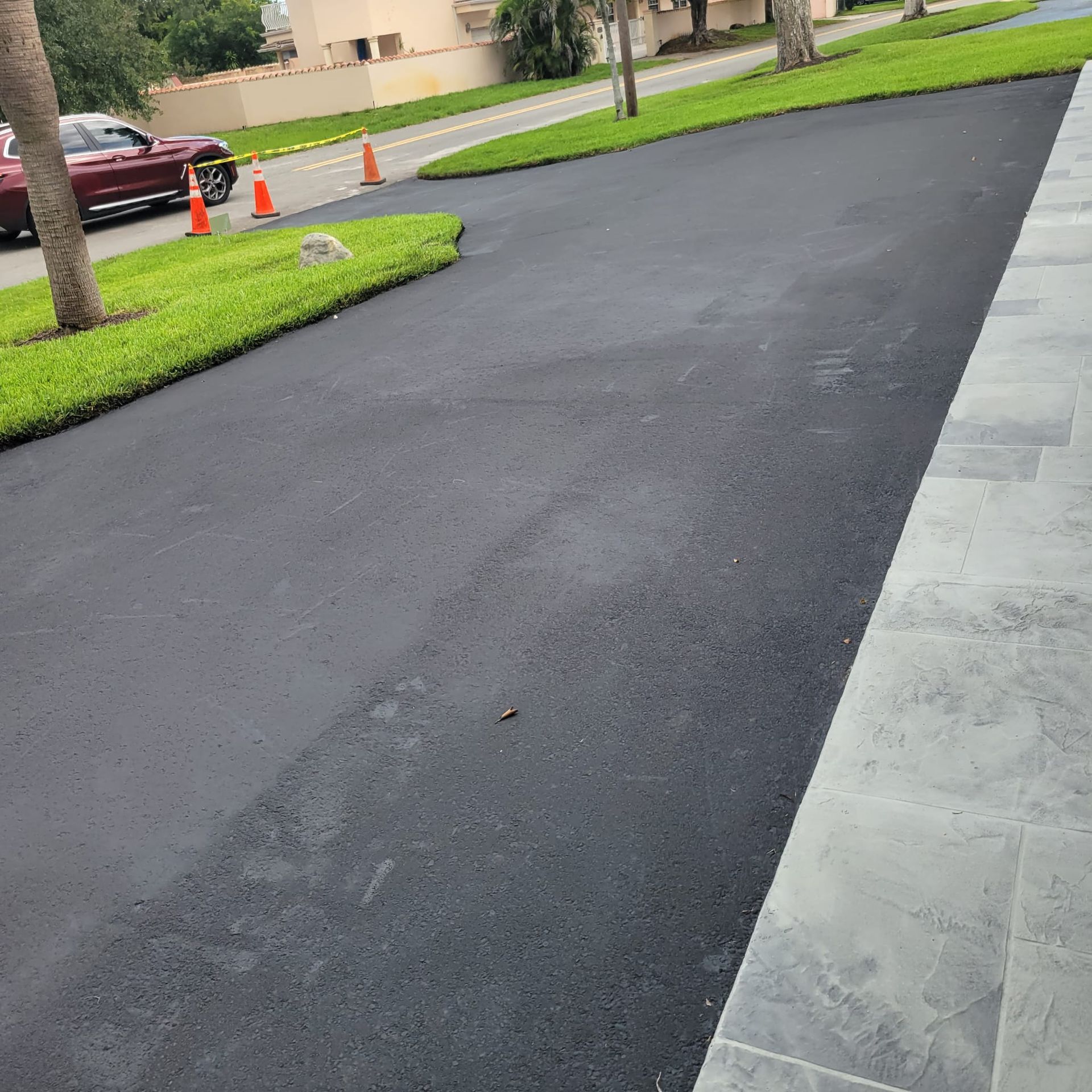 A worker operating a plate vibrator to compact a layer of fresh tarmac, repairing damage on an asphalt street.