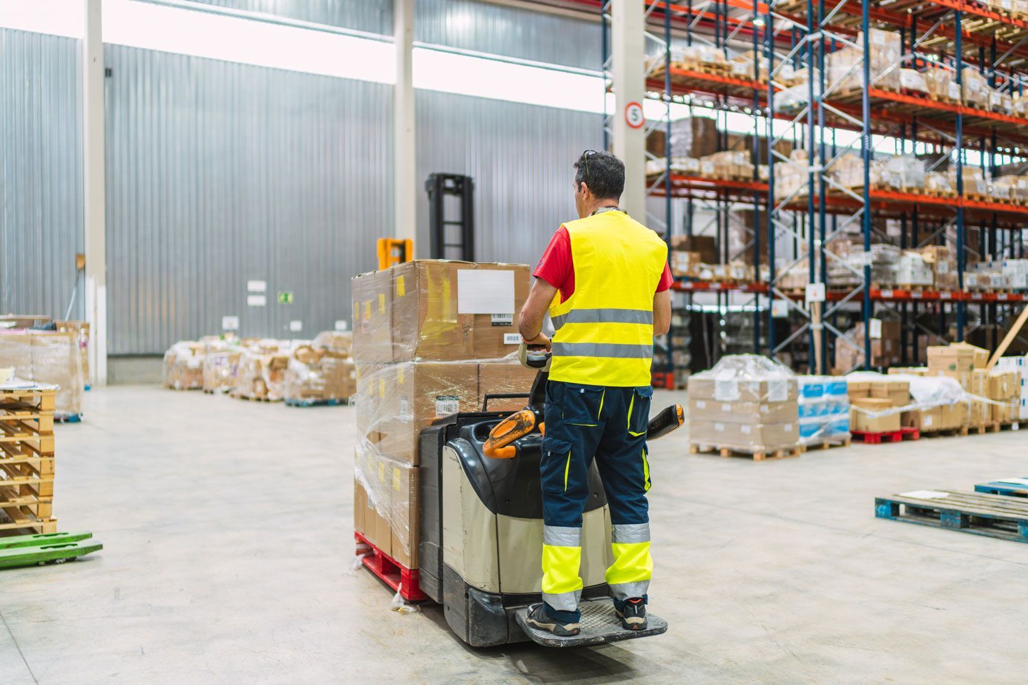 Warehouse worker driving a forklift beside stacked pallets and shelving