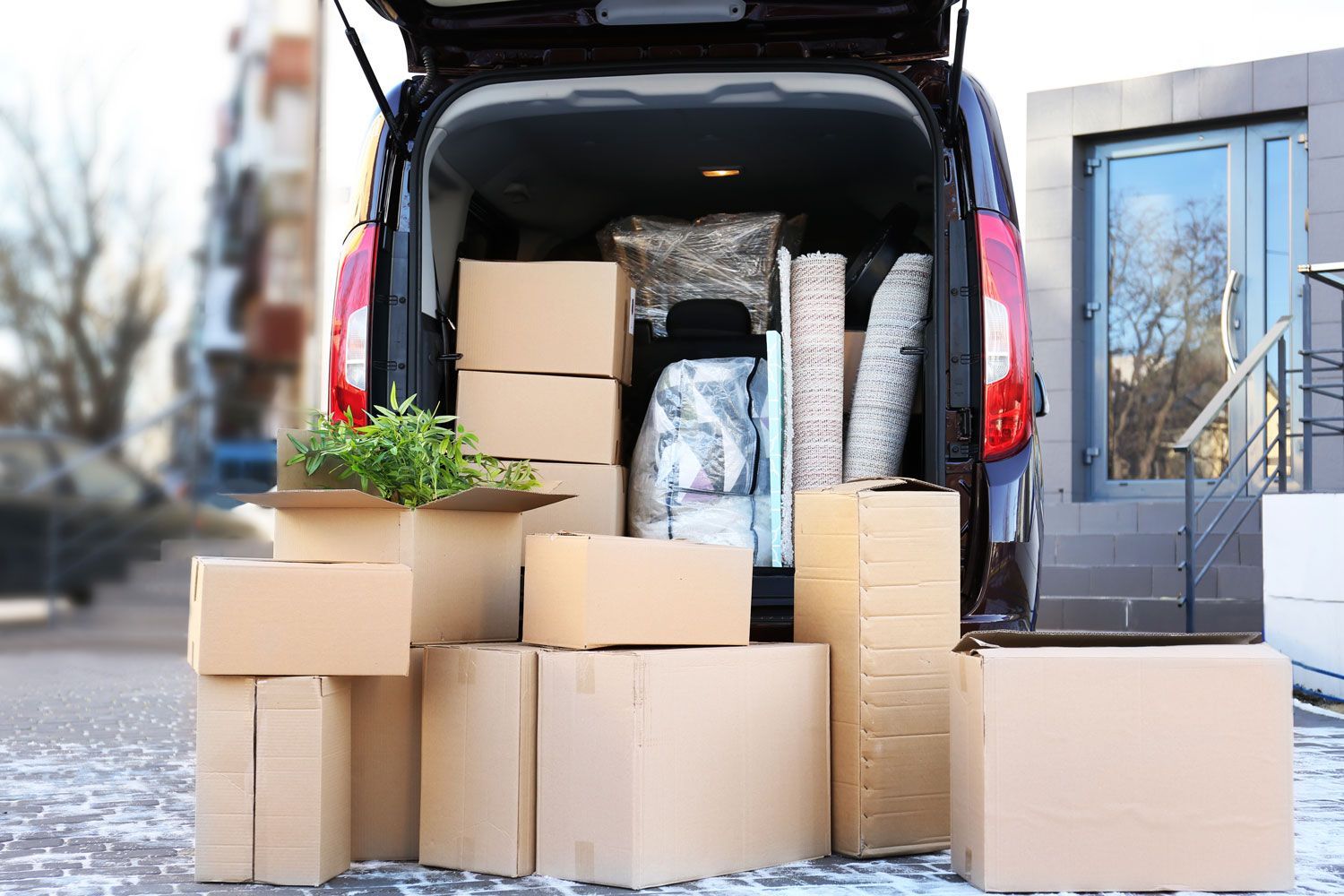 Open van with stacked moving boxes and packed household items outside a building