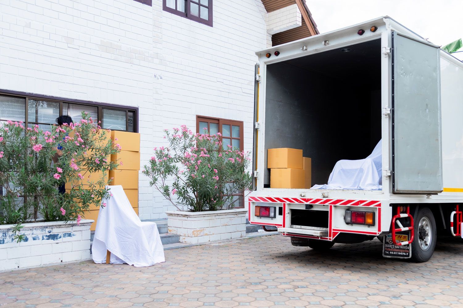 Moving truck parked by a white house, with boxes and furniture being loaded or unloaded.