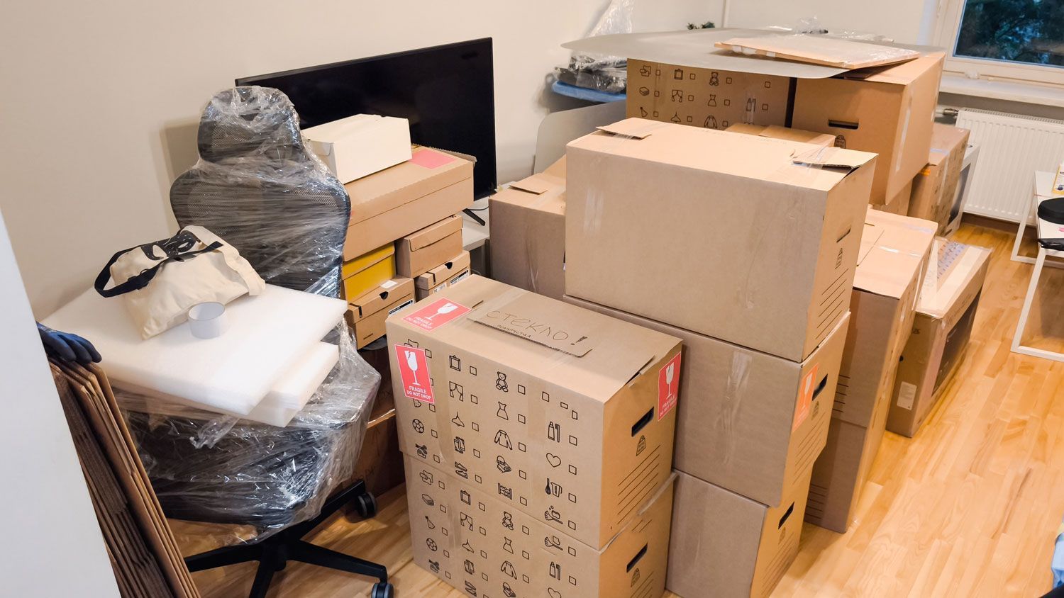Packed cardboard boxes and household items stacked in a room with hardwood floors