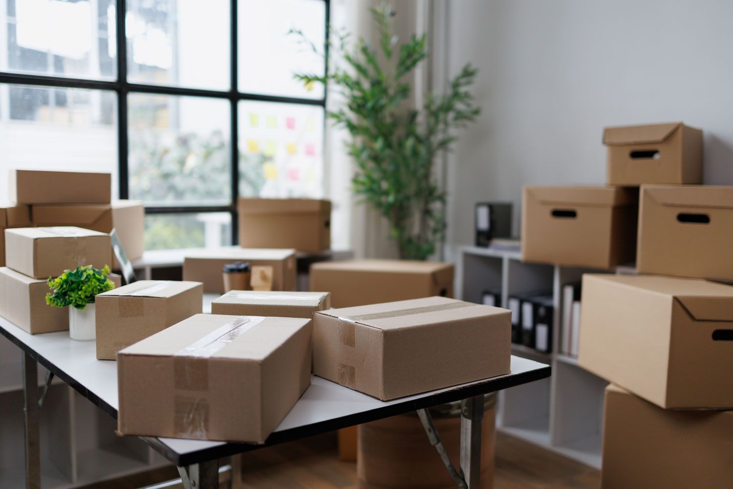 Cardboard boxes packed on tables in a bright office, suggesting a move or storage setup