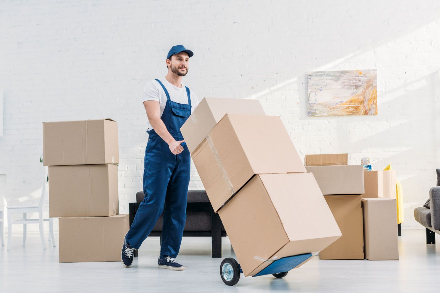 Mover pushing a dolly stacked with cardboard boxes in a bright warehouse