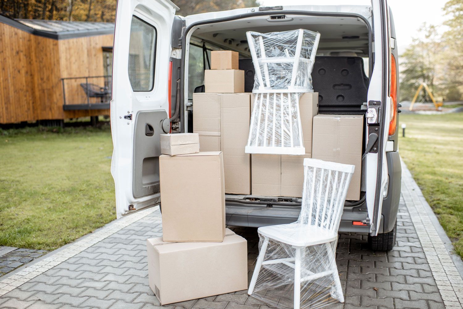 White van loaded with cardboard boxes and two chairs outside a house