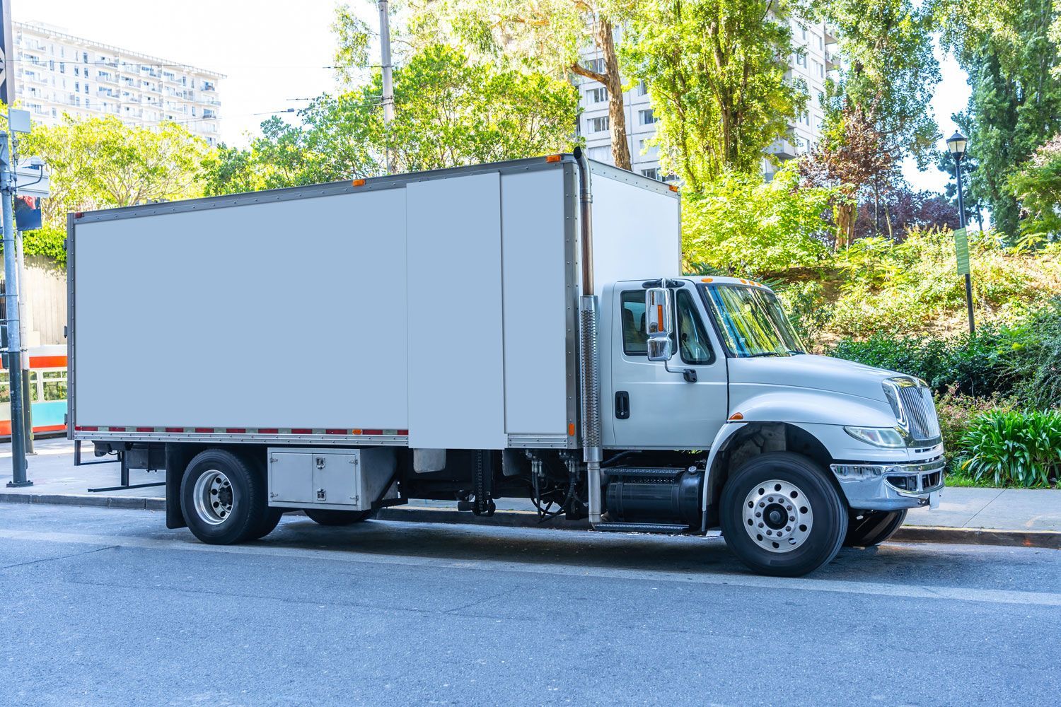 White box truck parked on a city street beside trees and buildings