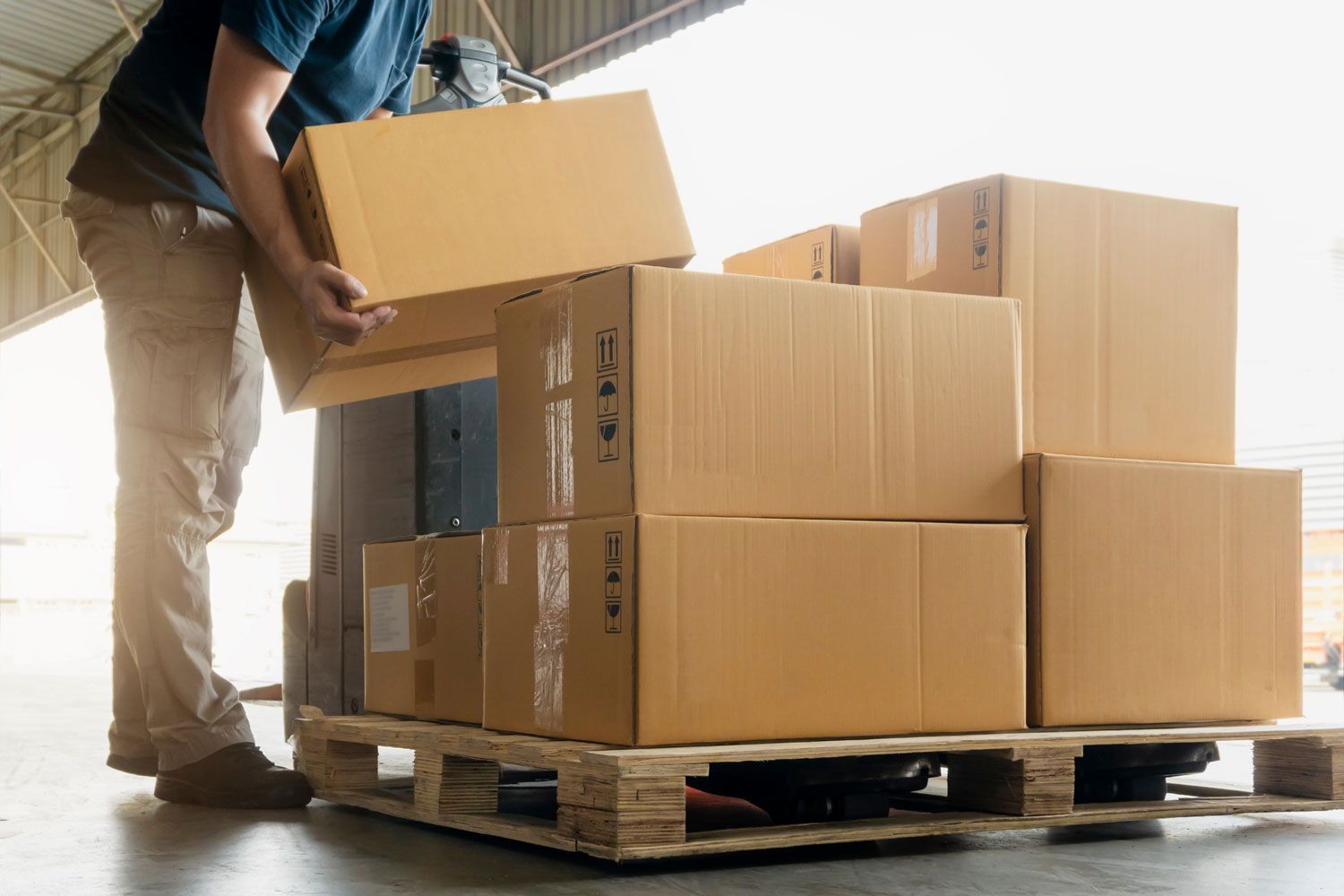Worker stacking cardboard boxes on a warehouse pallet near a loading dock