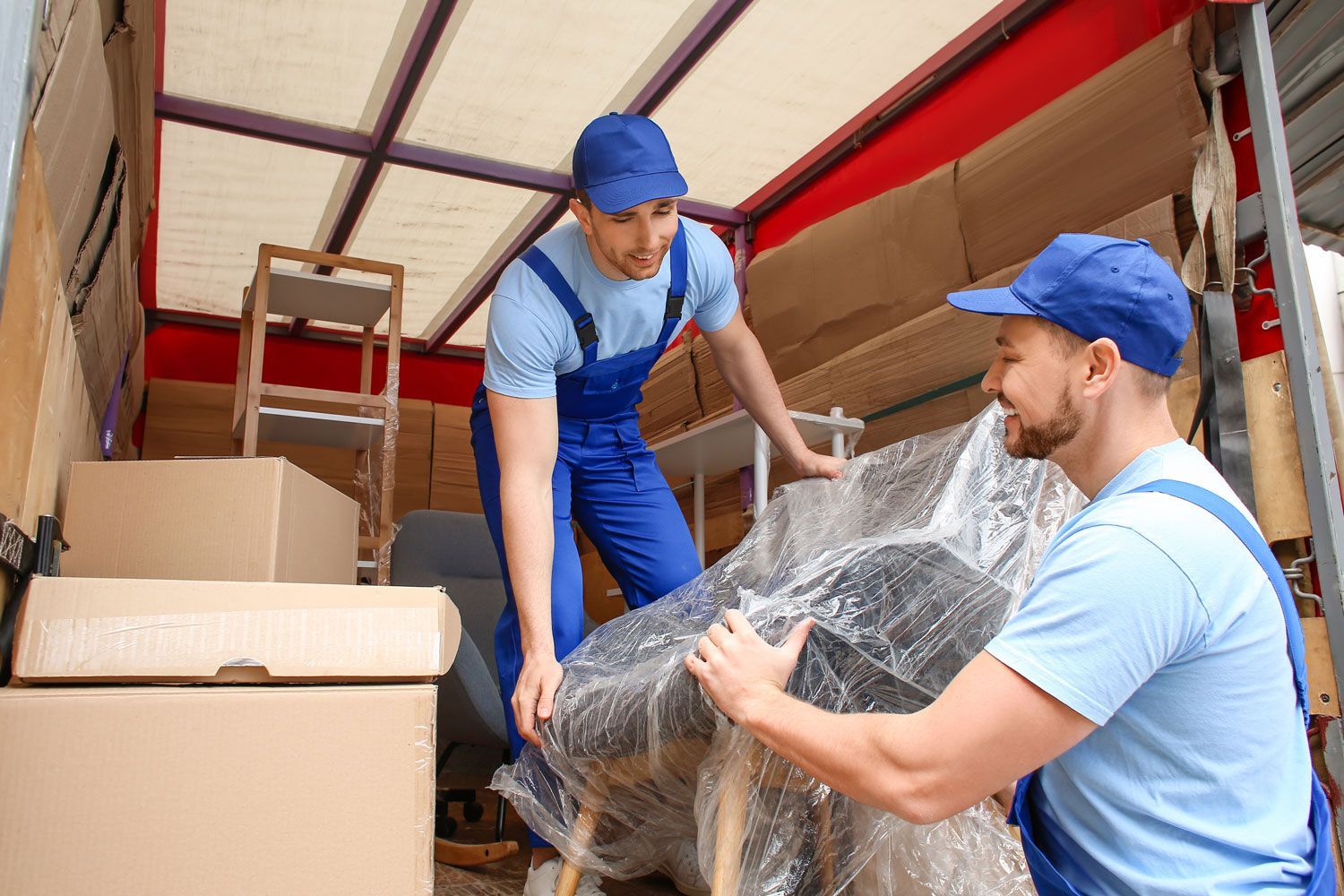 Two movers in blue uniforms loading a wrapped couch into a moving truck