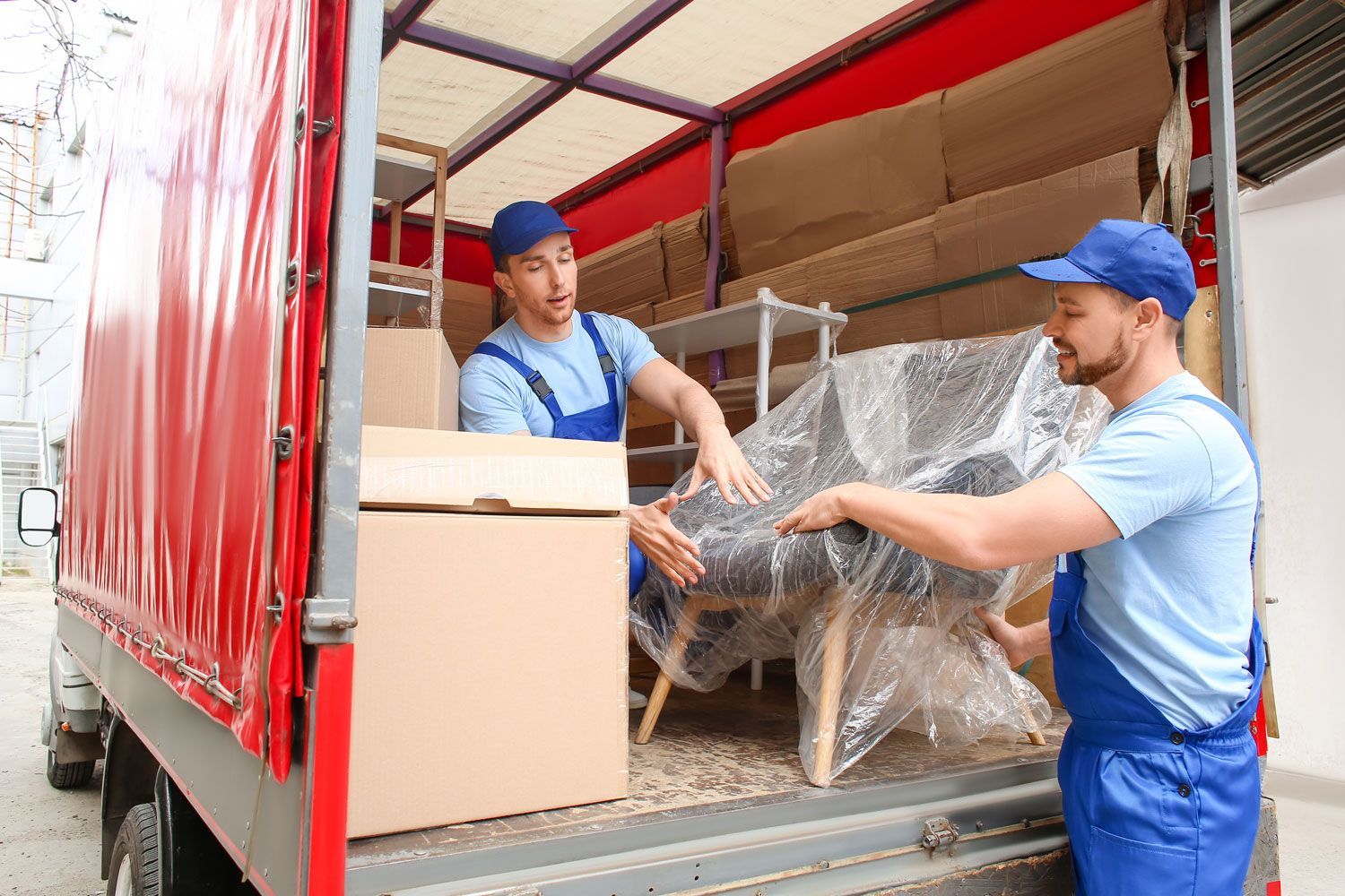 Two movers loading a truck with boxes and wrapped furniture at a warehouse dock