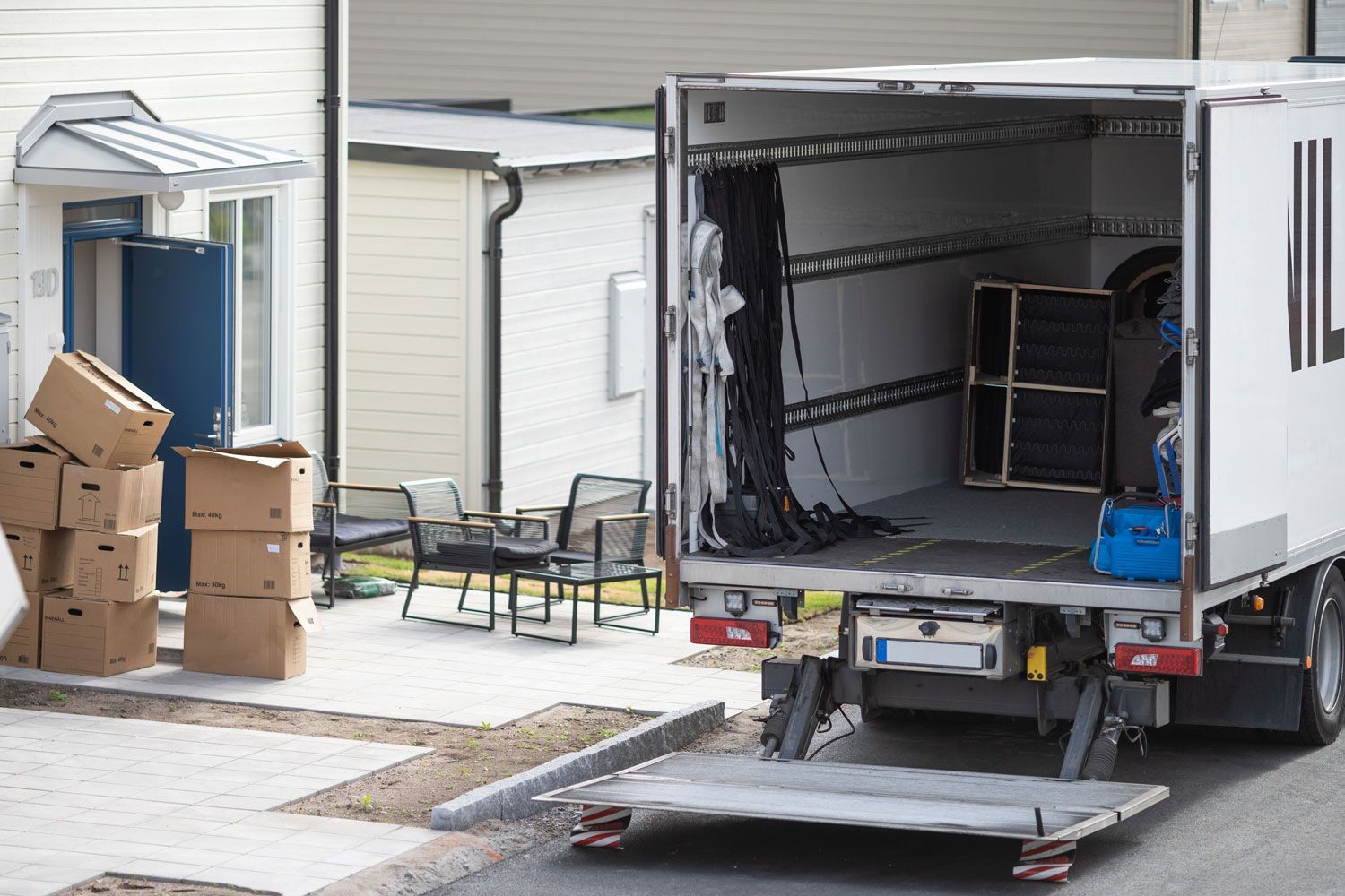 Moving truck with open cargo ramp beside stacked moving boxes outside a house