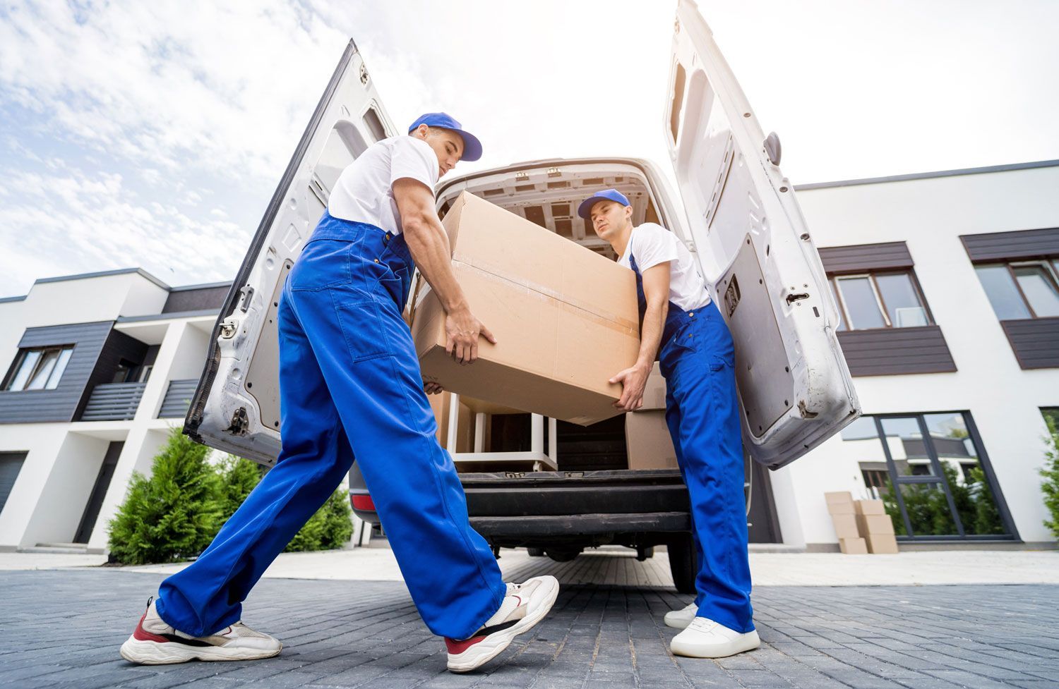 Two movers in blue uniforms carrying a cardboard box from a delivery truck