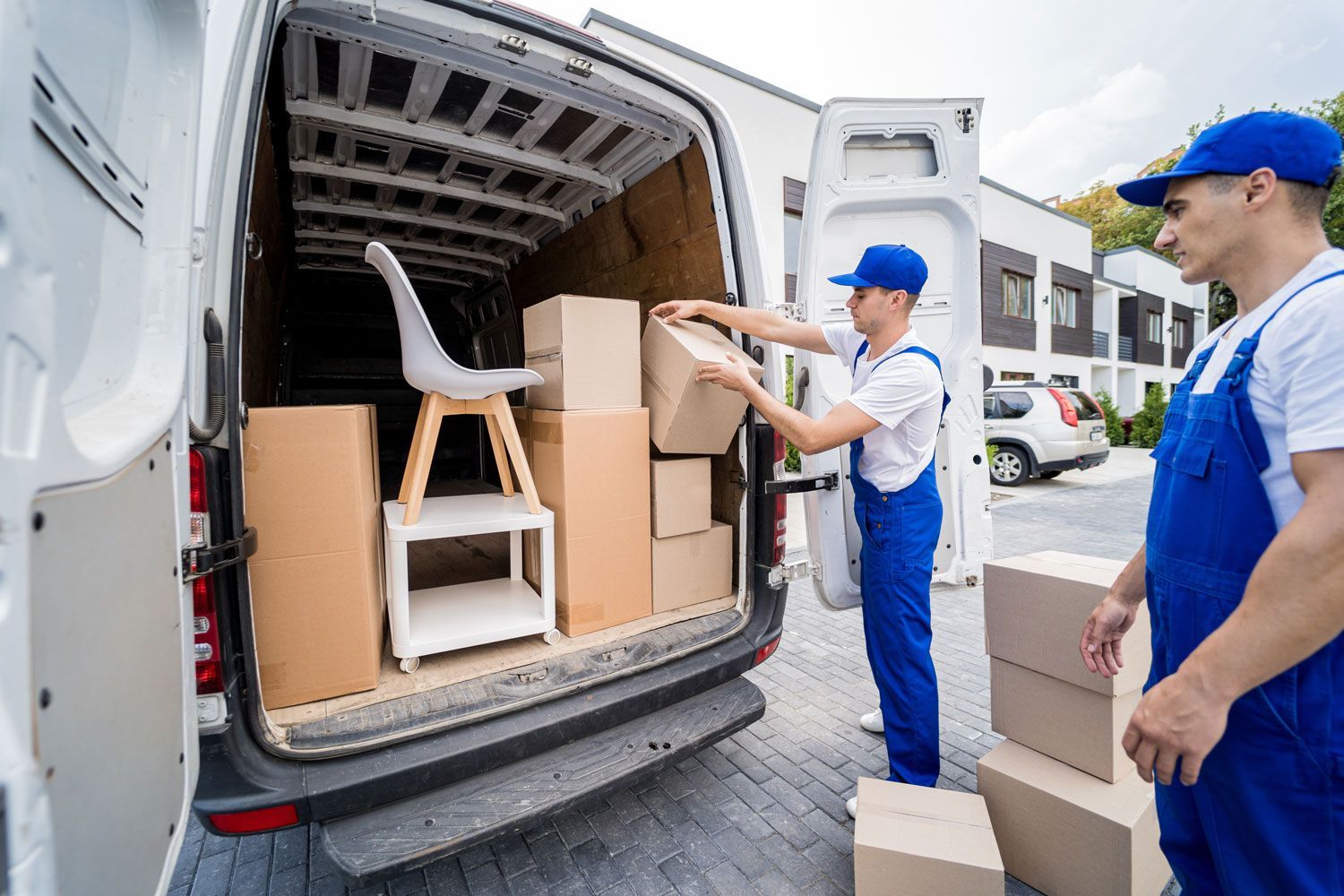 Two movers loading cardboard boxes into a white delivery van outdoors