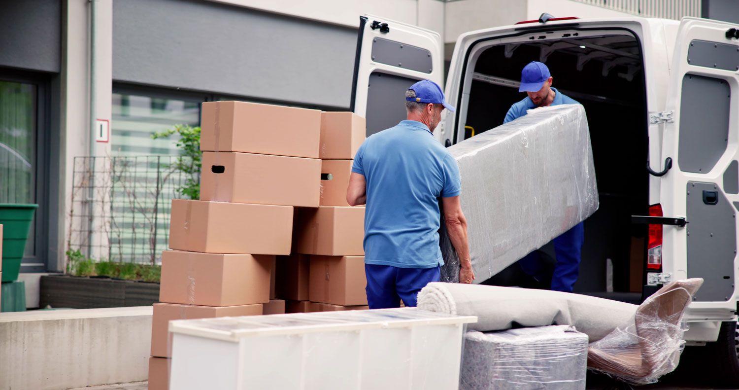 Movers loading boxes and wrapped furniture into a white delivery van outside a building