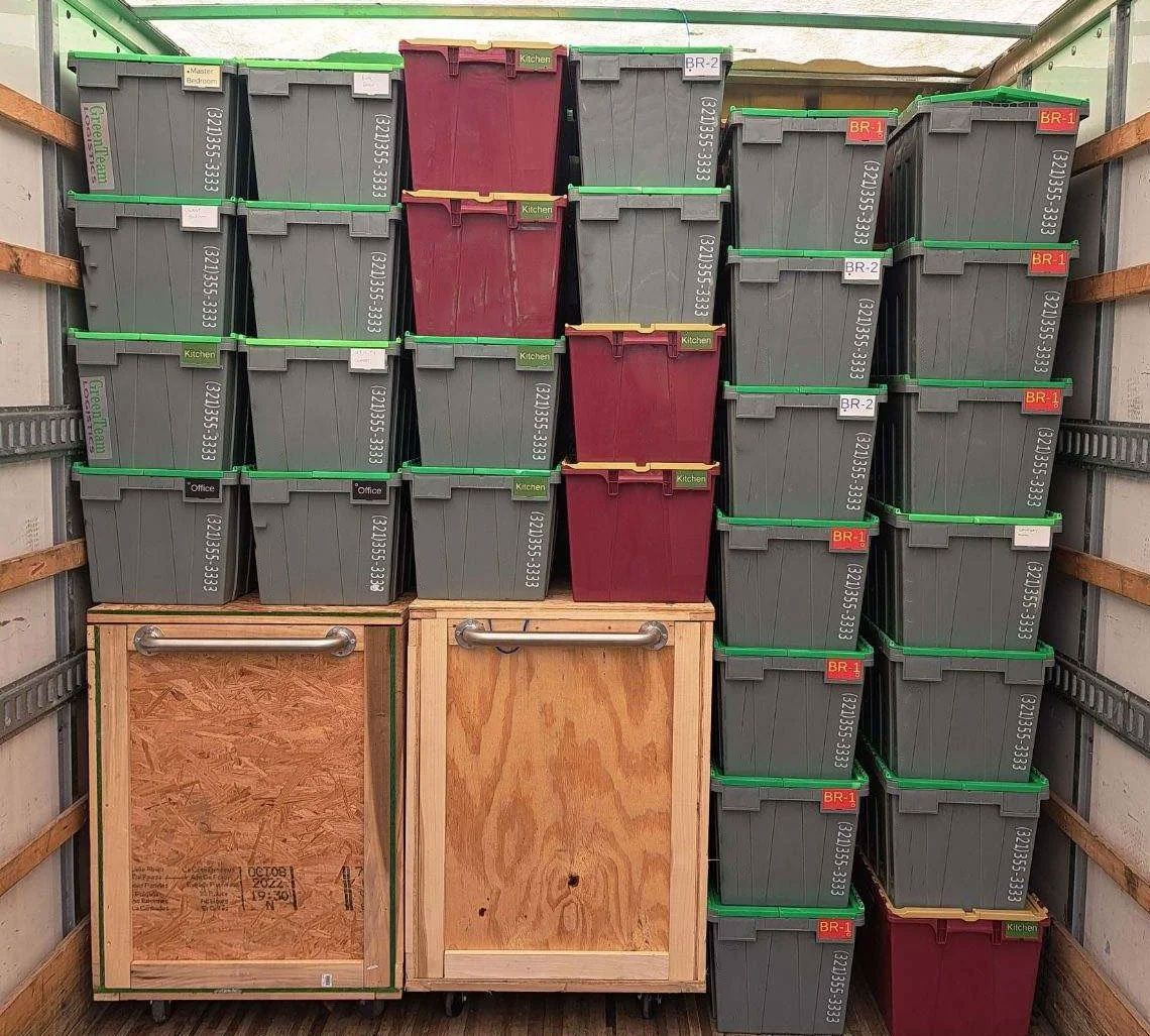 Stacked black and maroon storage bins in a truck, with two wooden crates in front.