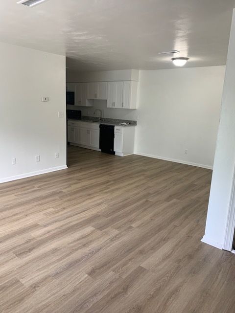 A living room with hardwood floors and a kitchen in the background.