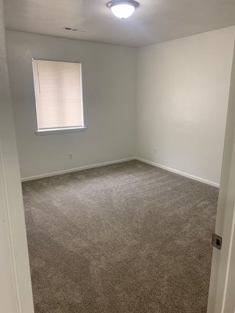 An empty bedroom with a carpeted floor and a window.