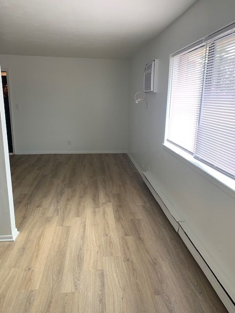 An empty living room with hardwood floors and two windows.