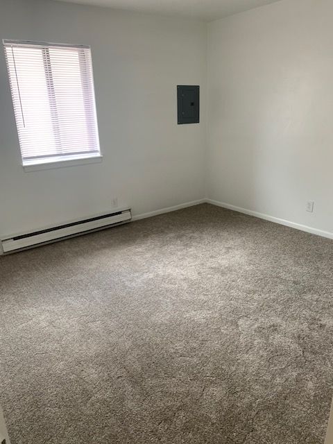 An empty bedroom with a large carpeted floor and a window.