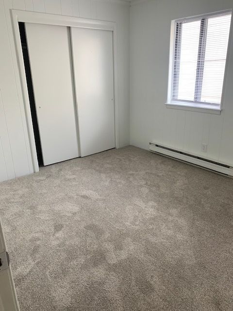 An empty bedroom with a carpeted floor and a window.