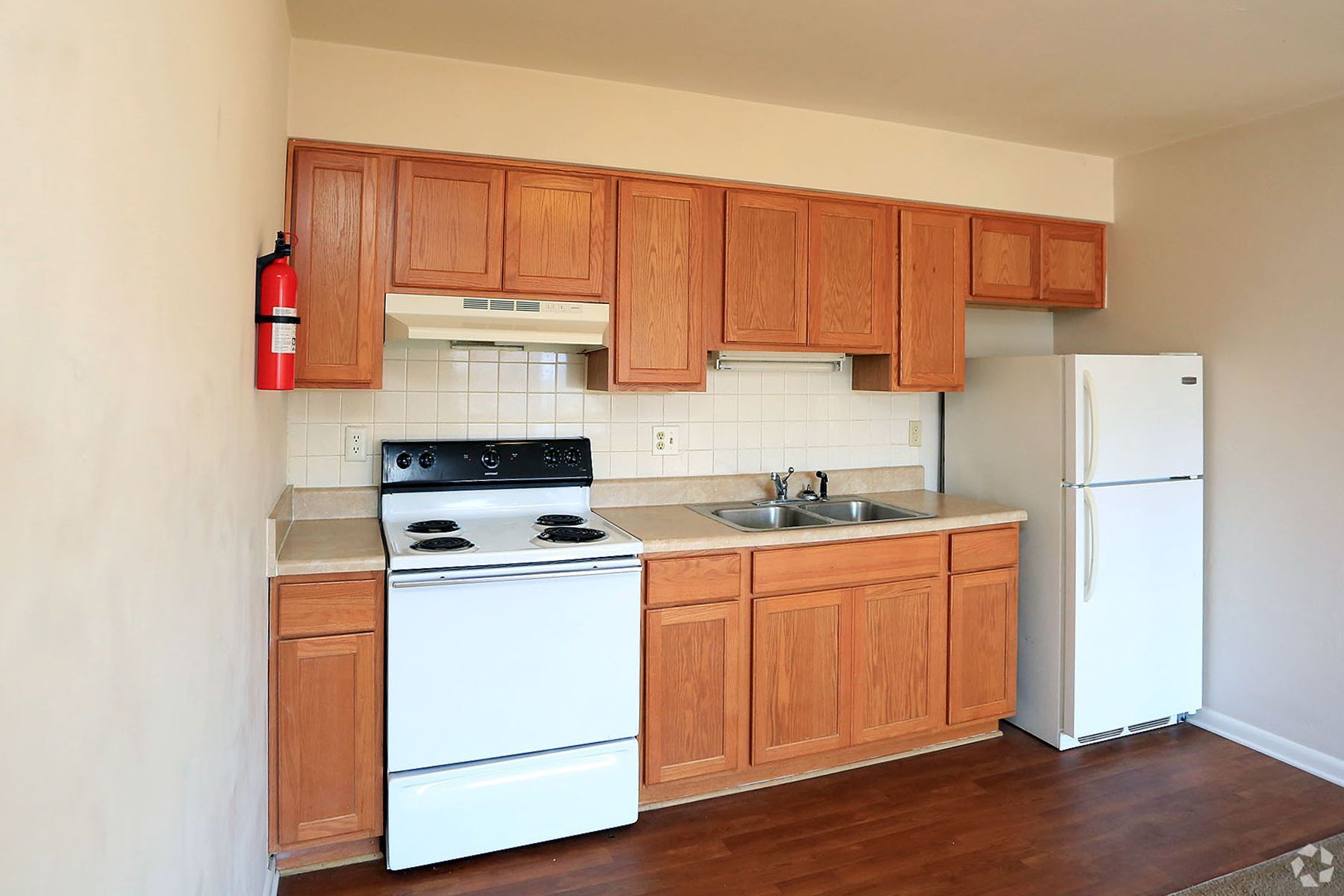 A kitchen with a stove , refrigerator , sink and fire extinguisher on the wall.