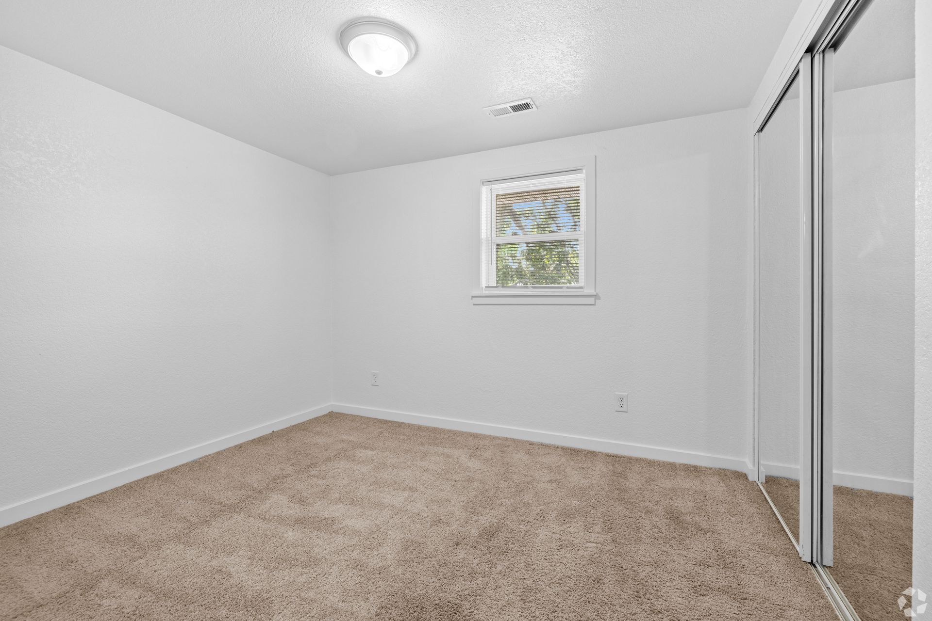 An empty bedroom with a picture on the wall and a sliding glass door.