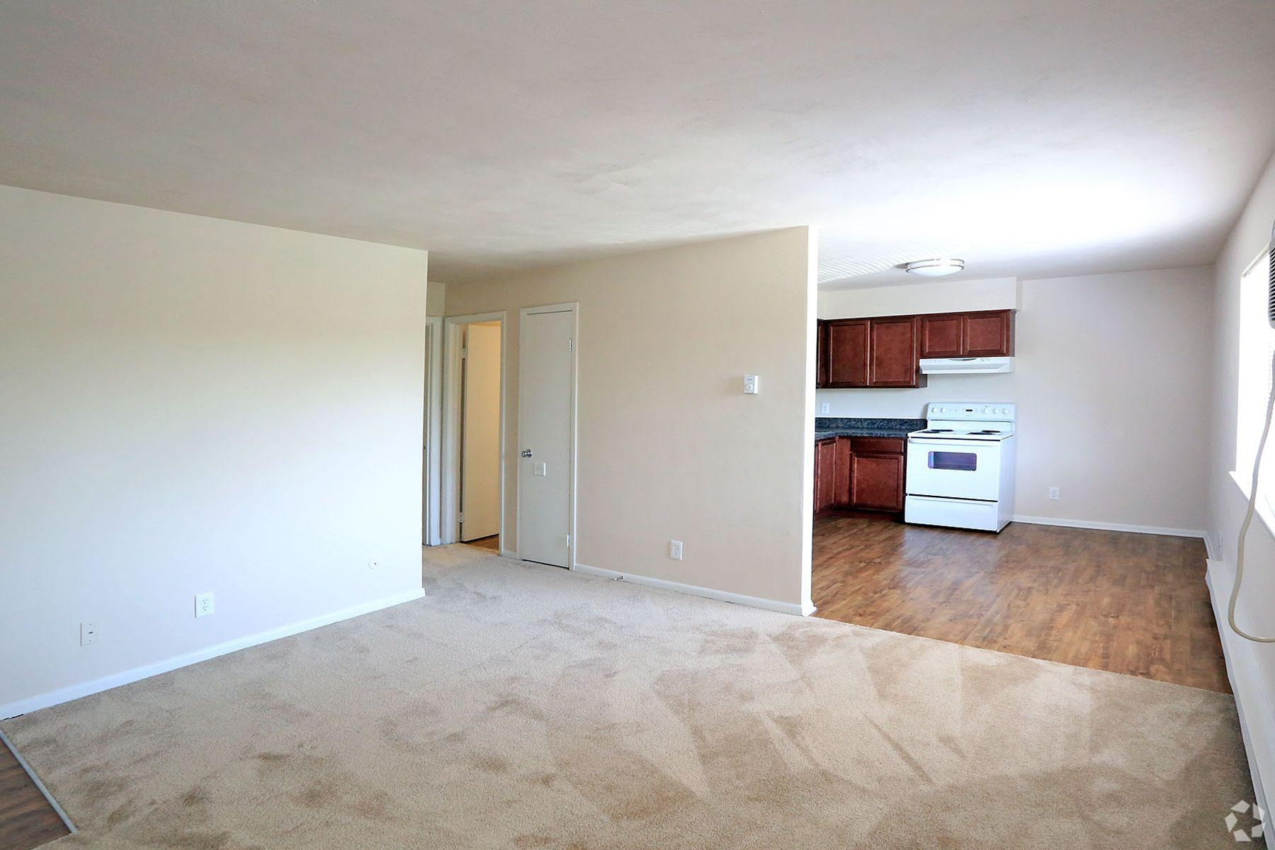An empty living room with a kitchen in the background