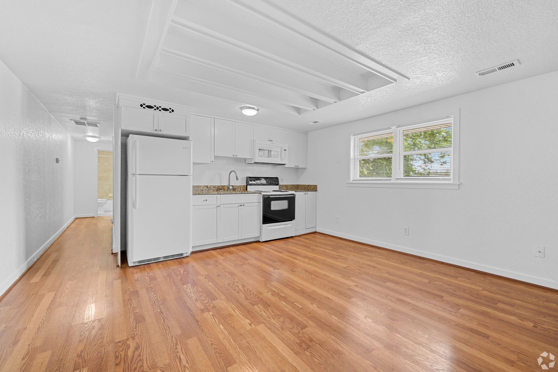 An empty living room with hardwood floors and a kitchen.
