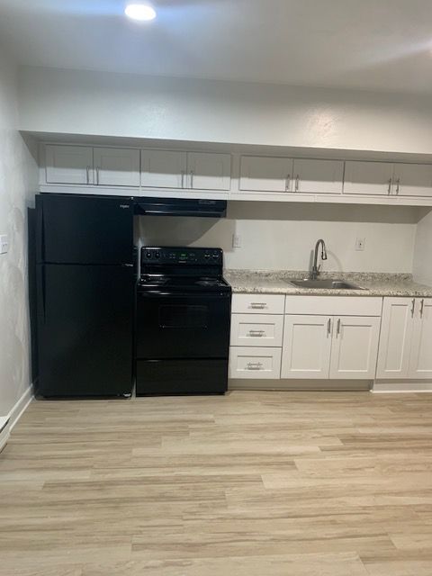 A kitchen with white cabinets , a black refrigerator , a black stove , and a sink.