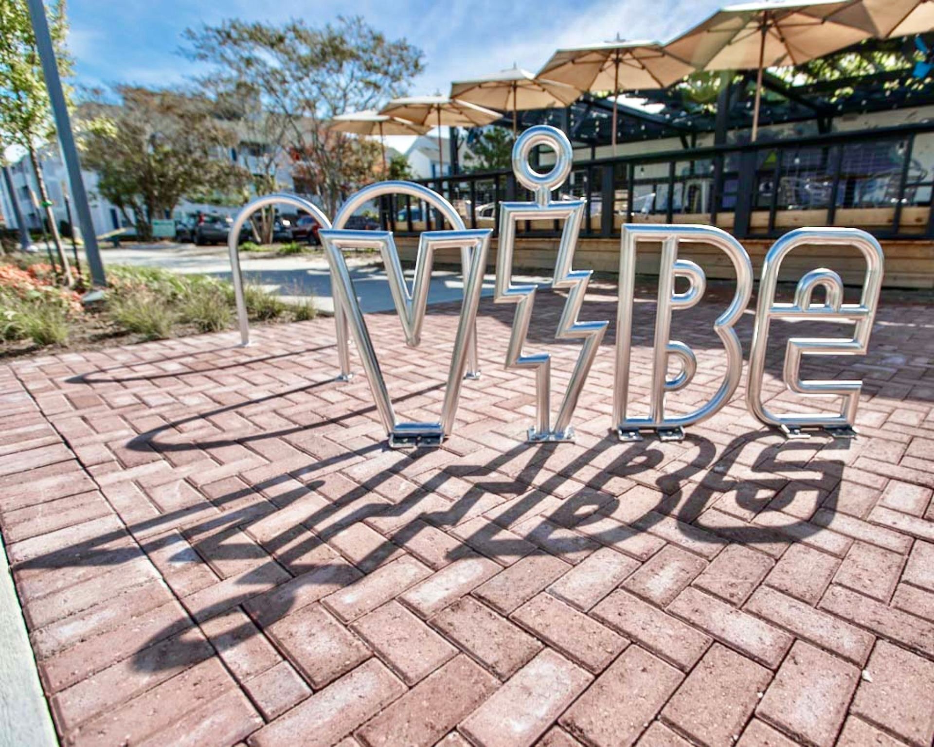 A bike rack with the word vibe on it is on a brick sidewalk.