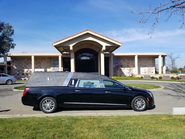 Black hearse parked in front of a building with a peaked entrance, under a clear blue sky