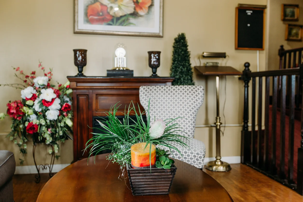 Living room with a wooden table, potted plant centerpiece, flowers, cabinet, and decorative chair
