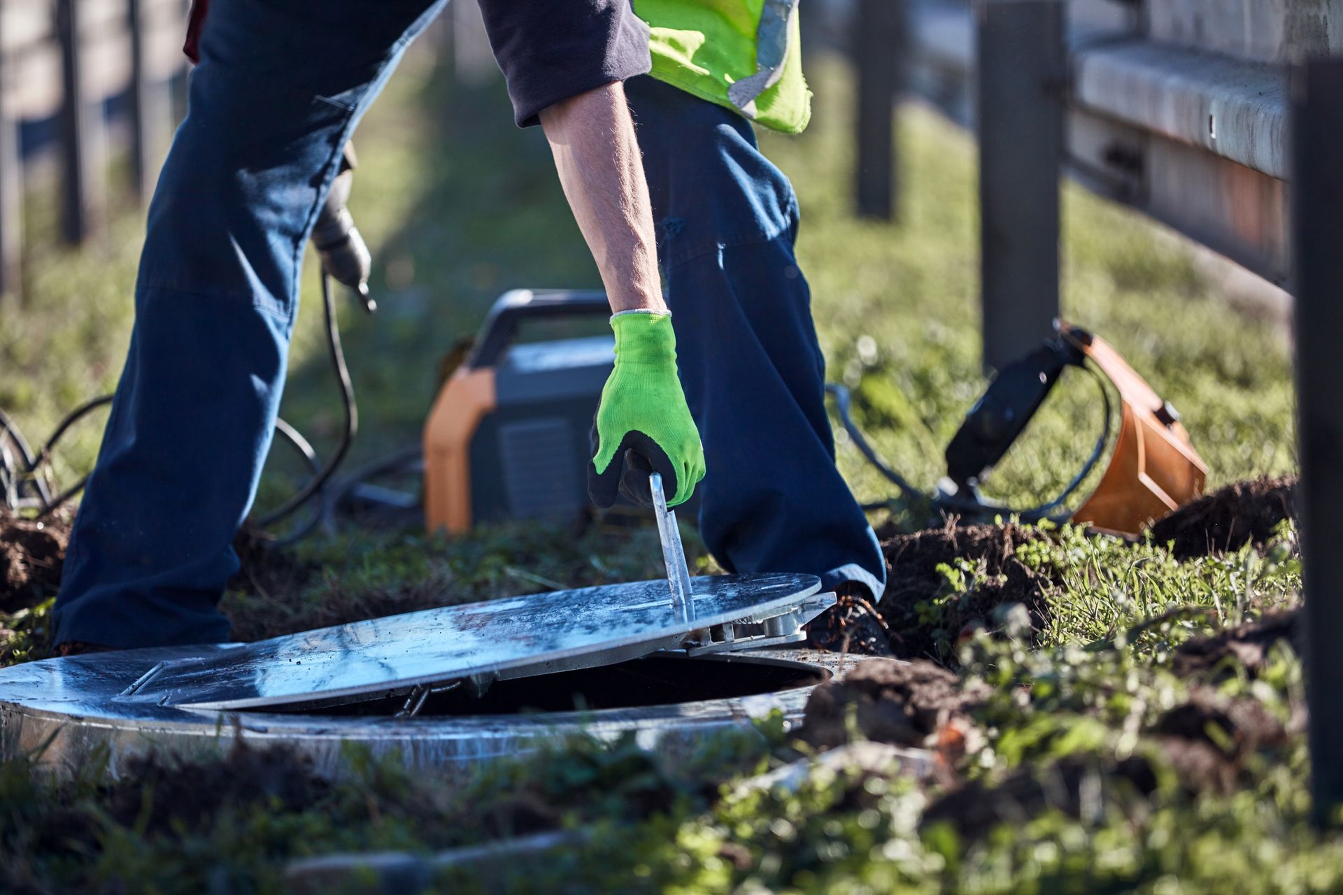 Worker in green gloves using a tool to cut debris near a storm drain outdoors