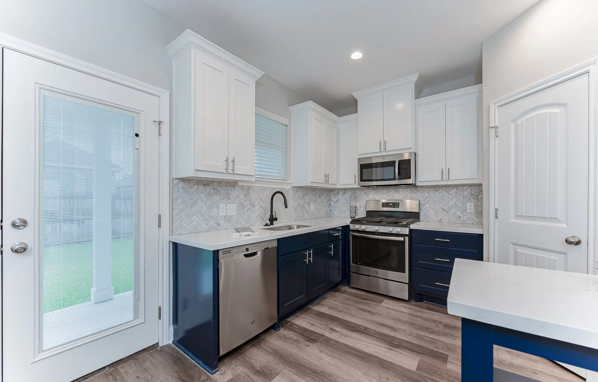 Kitchen with blue and white cabinets, stainless steel appliances, and a door to the outside.