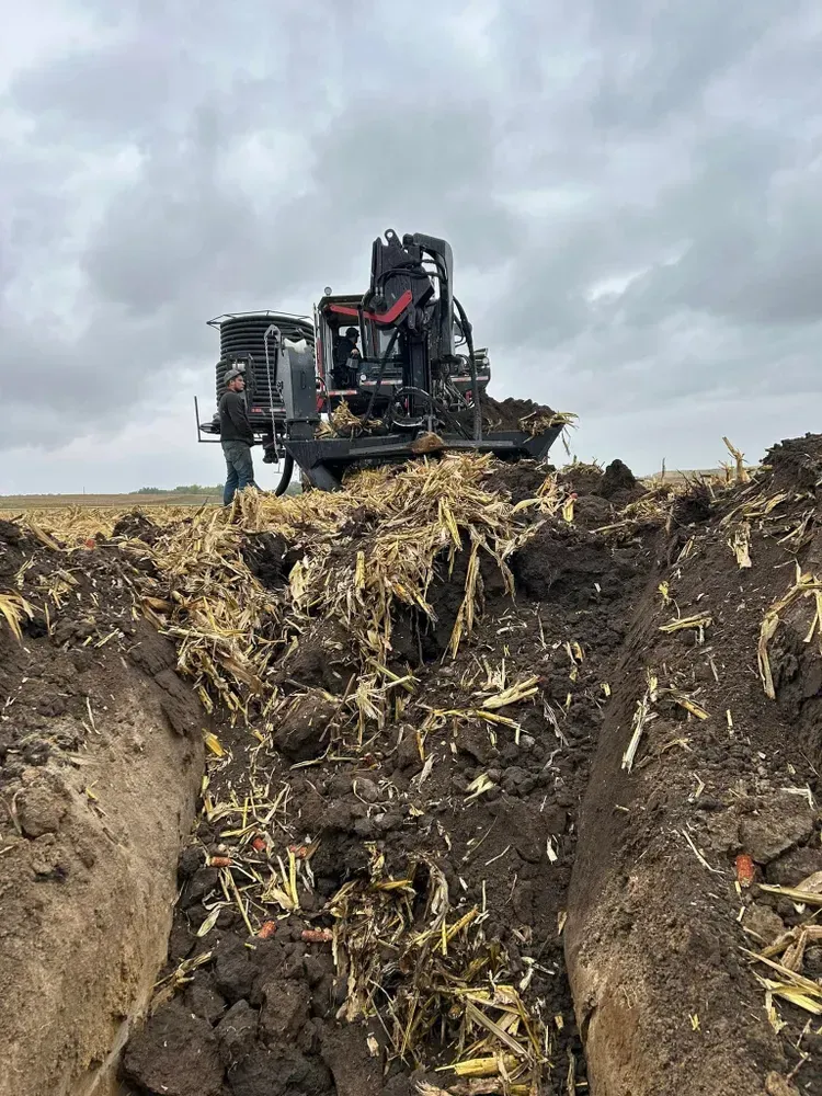 Heavy farm machine working in a muddy field under a cloudy sky