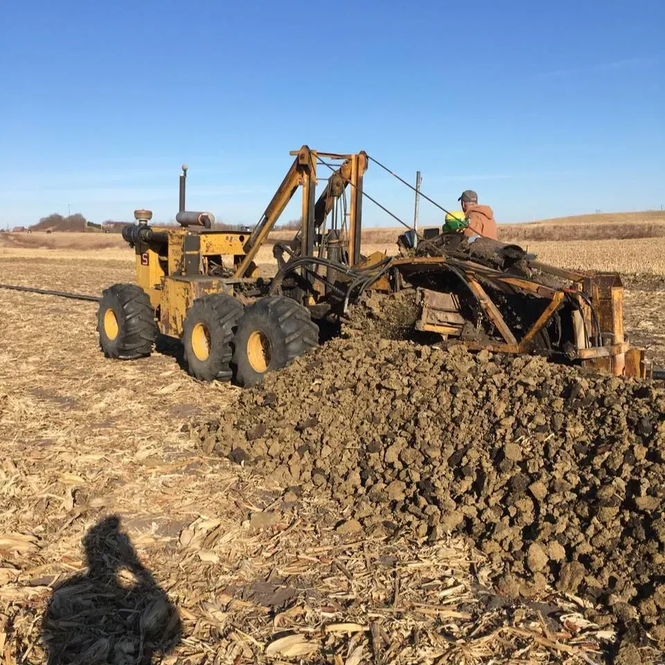 Yellow tractor scraping rocky soil in a dry field under a clear blue sky