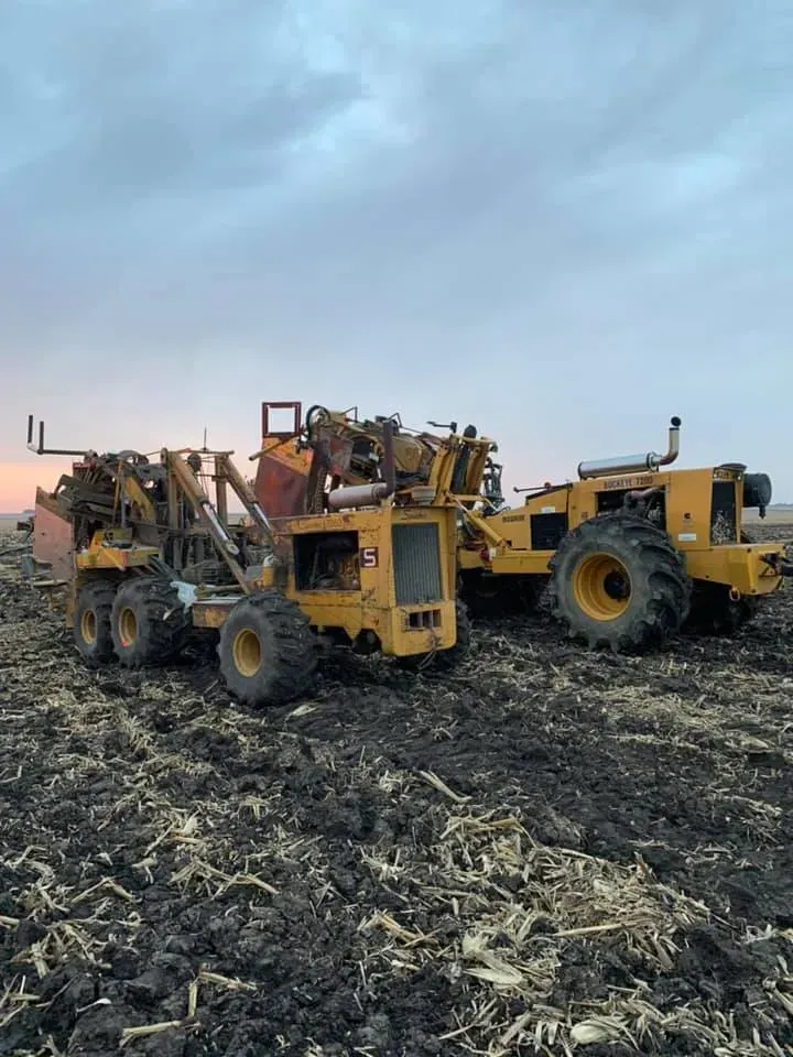 Two yellow industrial machines parked in a muddy field under a cloudy sky