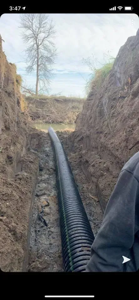 Black pipe running through a trench in a dirt hillside under a clear sky