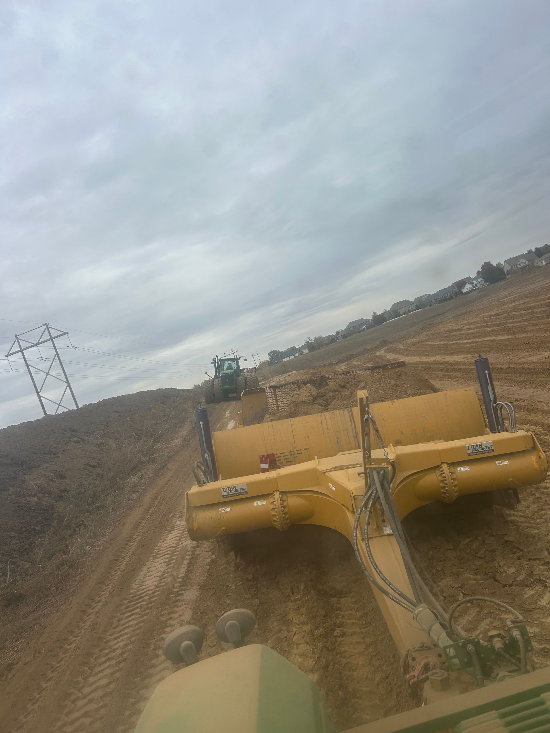 Yellow road grader working on a dirt road under a cloudy sky