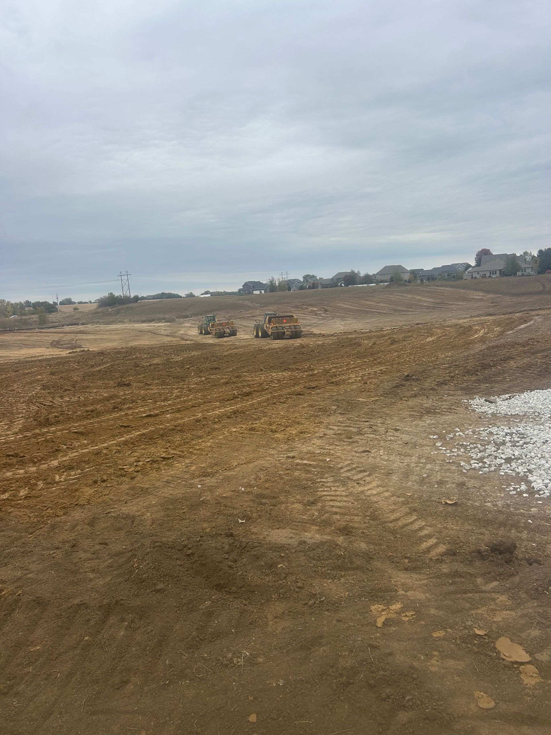Barren dirt field under a cloudy sky with a distant tree line and scattered houses