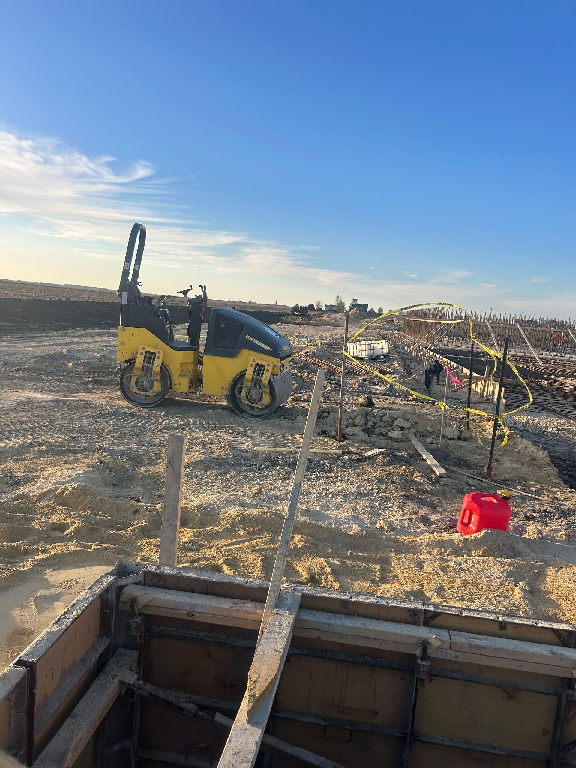 Yellow skid steer on a muddy construction site with a red bucket in the foreground under a blue sky
