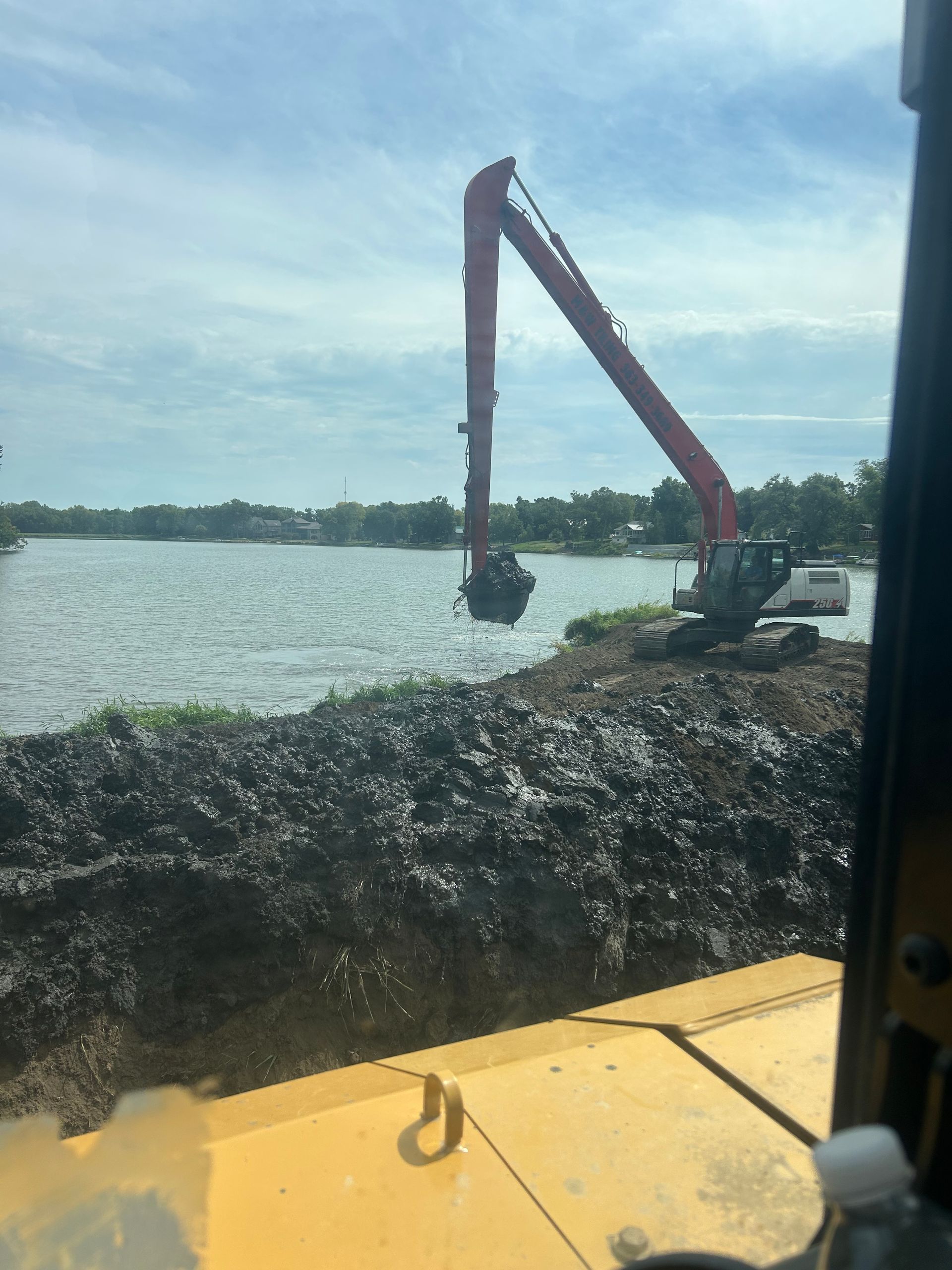 Excavator loading rocks from a barge on a lake under a clear sky