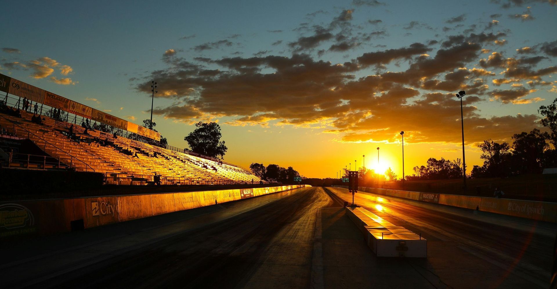 The sun is setting over a race track with a stadium in the background and Duda Builder