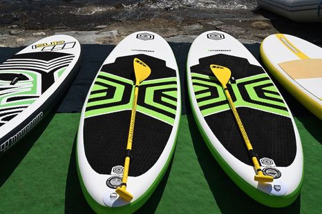 Row of white and black paddleboards with neon green and yellow graphics on a green surface